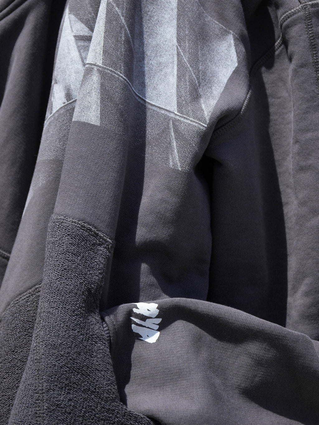 Close-up of a dark gray jacket with brutalist print and brand logo.